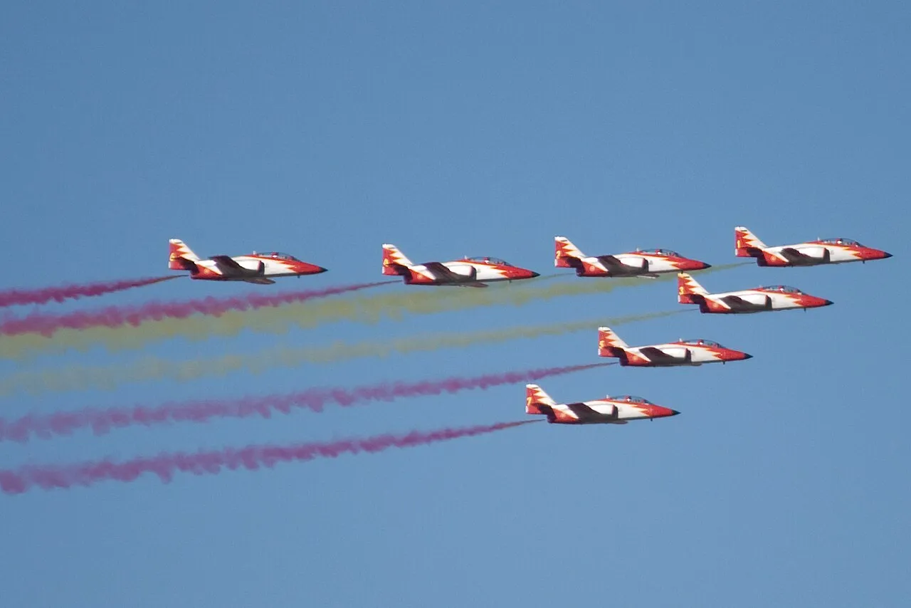 Toestellen van de Patrulla Águila vliegen boven Madrid tijdens het defilé van de Día de la Hispanidad, met rookpluimen in de kleuren van de Spaanse vlag.